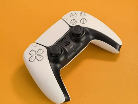 Manette Sony DualSense blanche et noire vue de dessus sur un fond orange