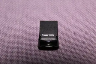 Boîtier noir d’une clé USB SanDisk Ultra Fit, photographié de face sur un tissu violet