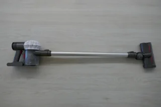 Ancien aspirateur balai Dyson V6 gris posé sur un sol clair ; photo illustrative, pas la photo exacte de Dreame Z30 ni preuve des accessoires fournis