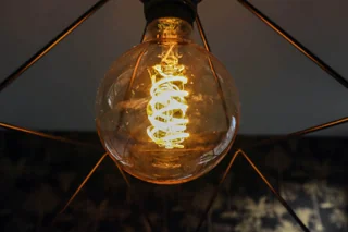 Une ampoule globe à filament allumée dans un luminaire ajouré ; photo illustrative, pas le modèle exact Philips Hue Play Gradient Light Tube compact noir ni preuve du coffret fourni