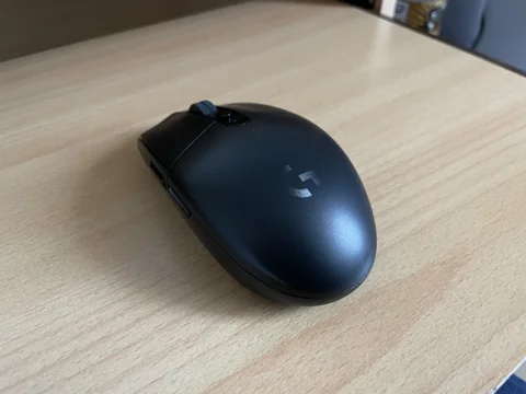 Souris Logitech G305 noire photographiée de trois quarts sur un bureau en bois